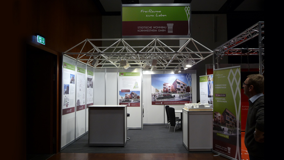 Beleuchteter Messestand mit Plakaten zur Vorstellung des Immobilienprojektes