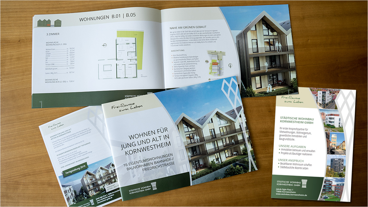 Titel und Doppelseite eines Exposés sowie eine Anzeige in DIN A5 auf einem Holztisch